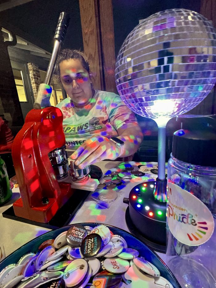 A volunteer makes buttons at a button press beside a glowing disco ball.